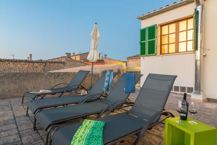 Una terraza en la azotea con asientos reclinables y una sombrilla cerrada.