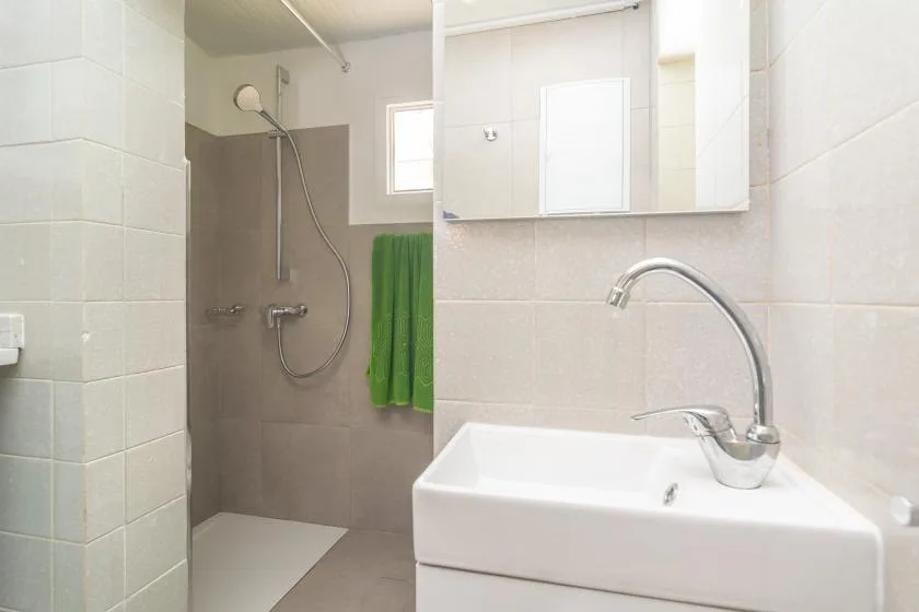 Un baño luminoso con ducha, lavabo y toalla verde.