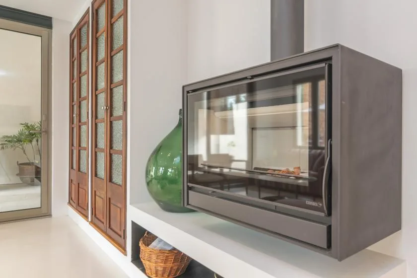 Una chimenea moderna está junto a ventanas altas con marcos de madera.