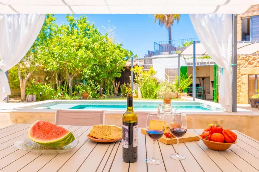 Una mesa junto a la piscina está preparada con fruta, pan y bebidas.