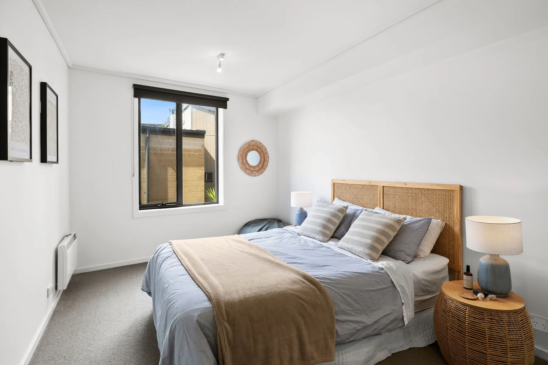 Un dormitorio luminoso con una cama, cabecero tejido y ventana.