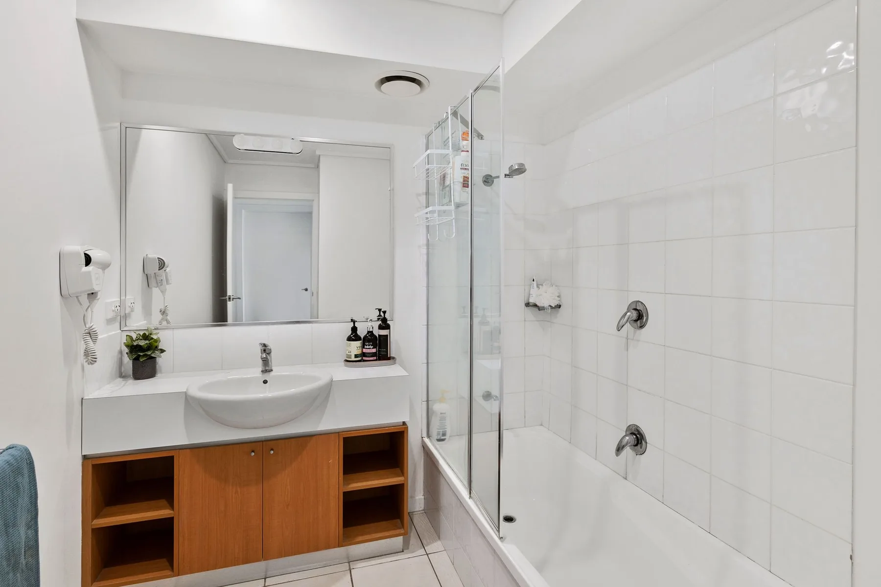 Un baño alicatado con lavabo y una ducha con mampara de vidrio.