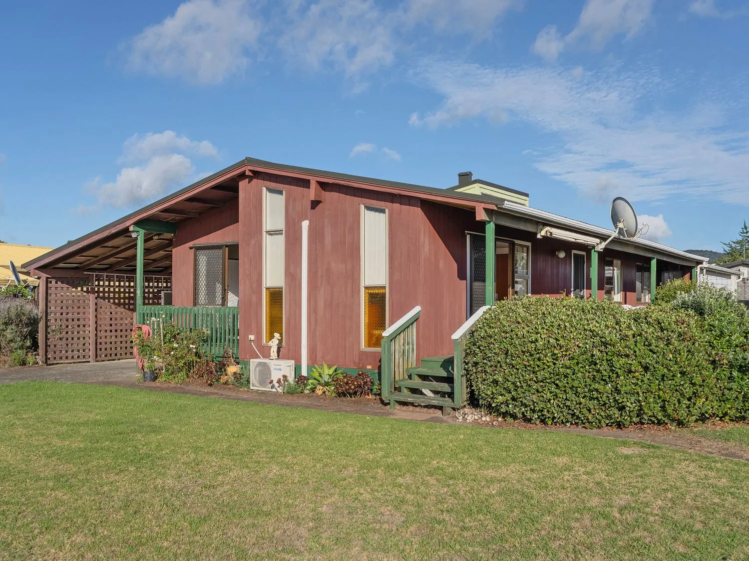 A brown house with green trim and a covered carport on a lawn at Golden Days - Whitianga Holiday Home in Whitianga
