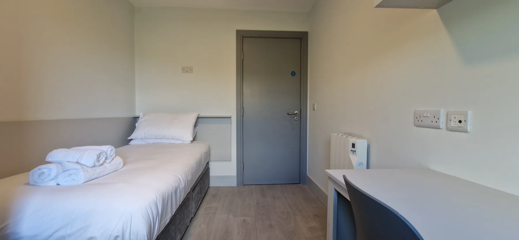 A bedroom with a single bed and a desk beside the door.