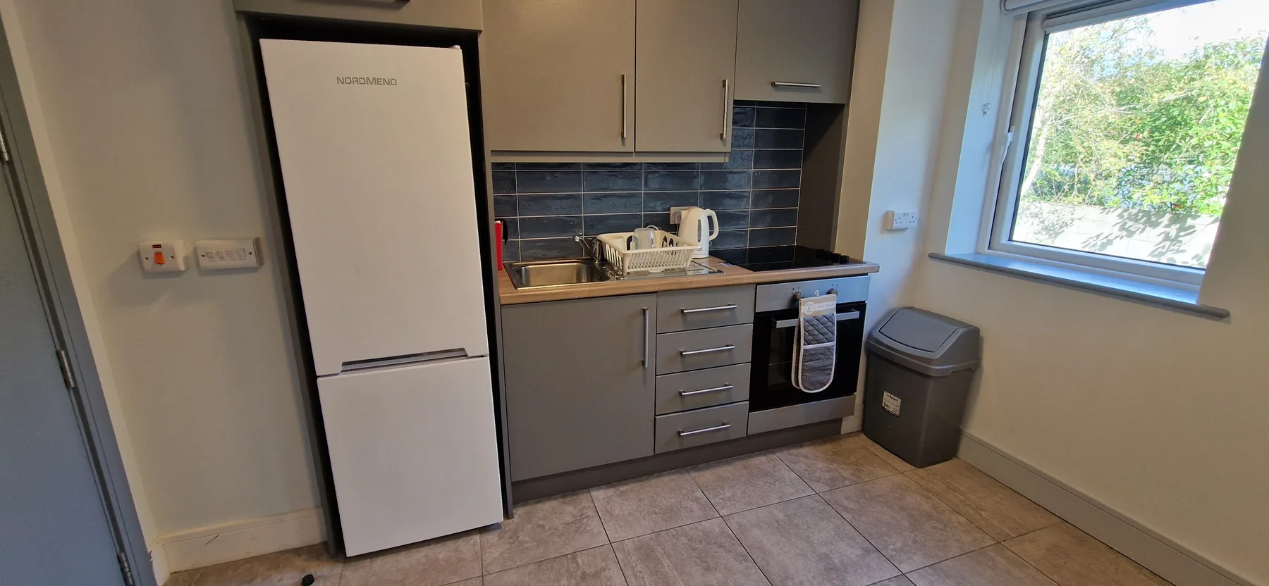 A compact kitchen with gray cabinets, appliances, and a window.