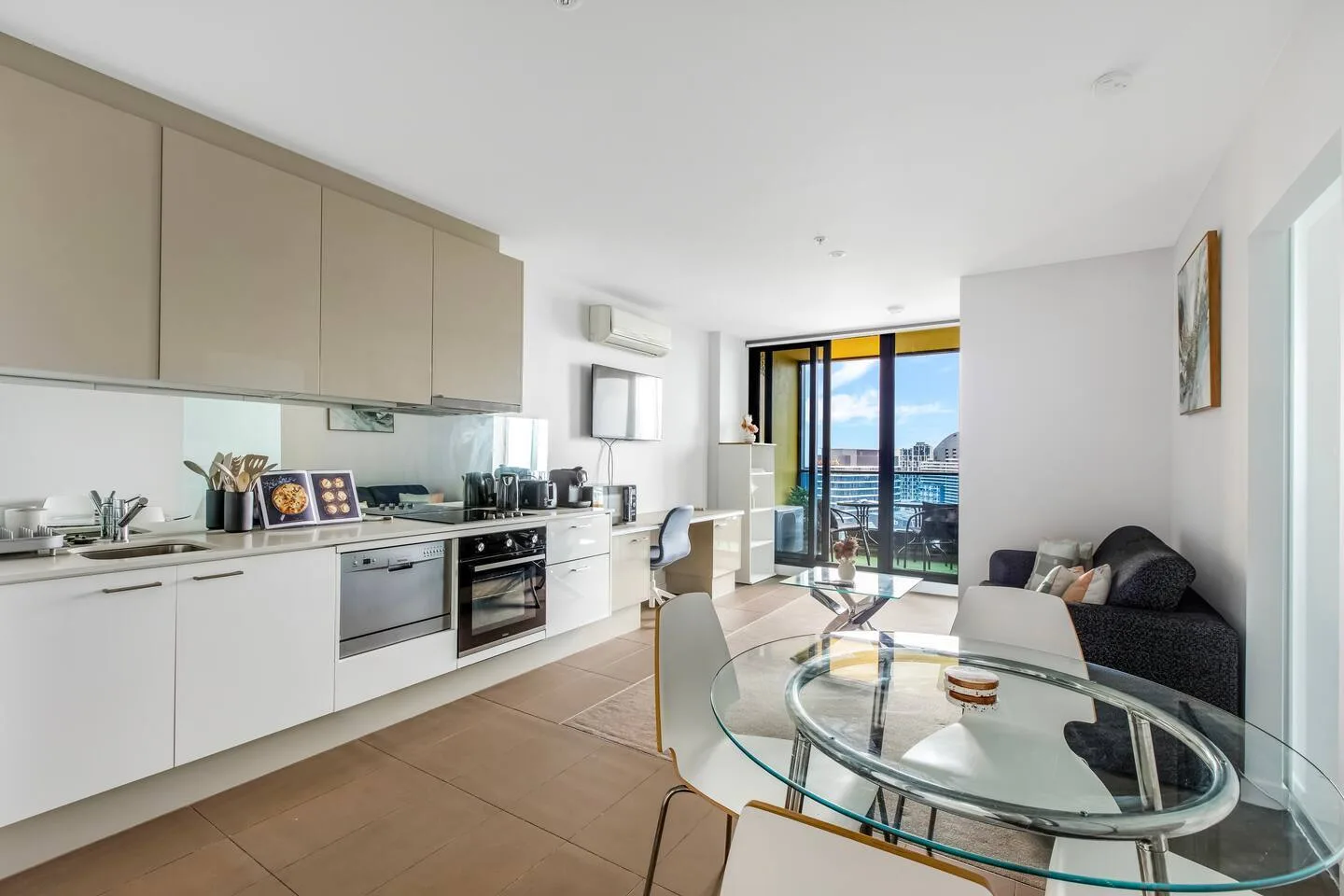 A bright open-plan kitchen and living area has a glass dining table beside the seating.