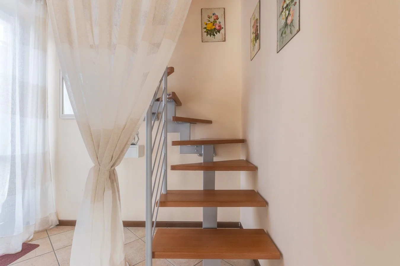 A wooden staircase with metal railing rises beside a sheer curtain.