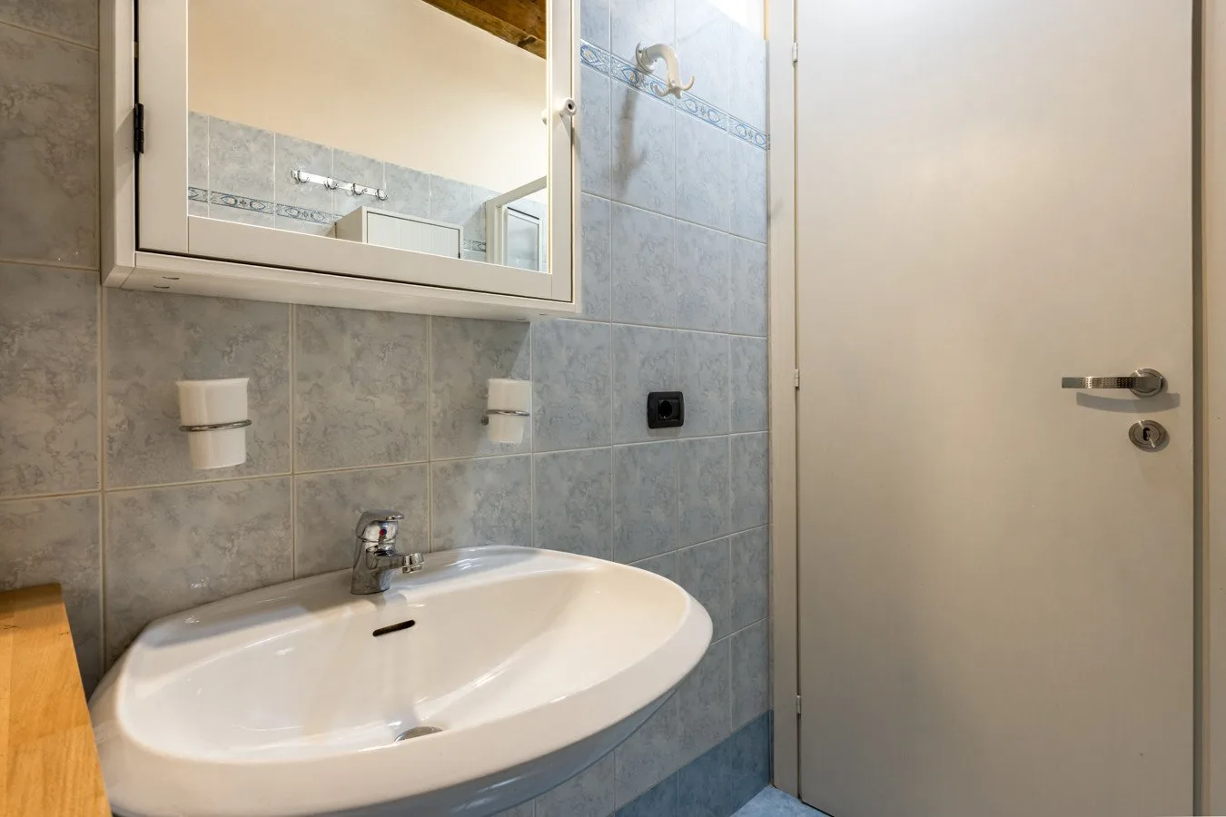 A tiled bathroom with a wall-mounted sink and mirror.