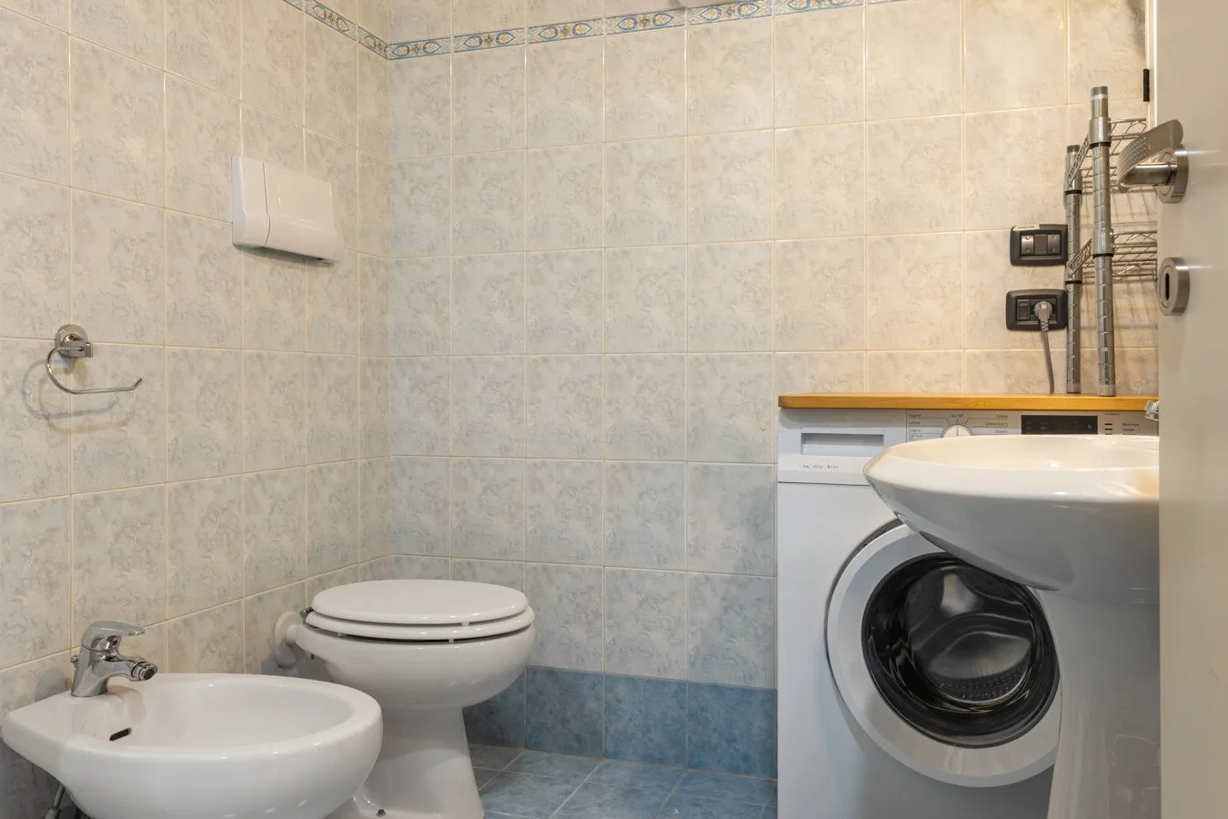A tiled bathroom with a toilet, bidet, sink, and washing machine.