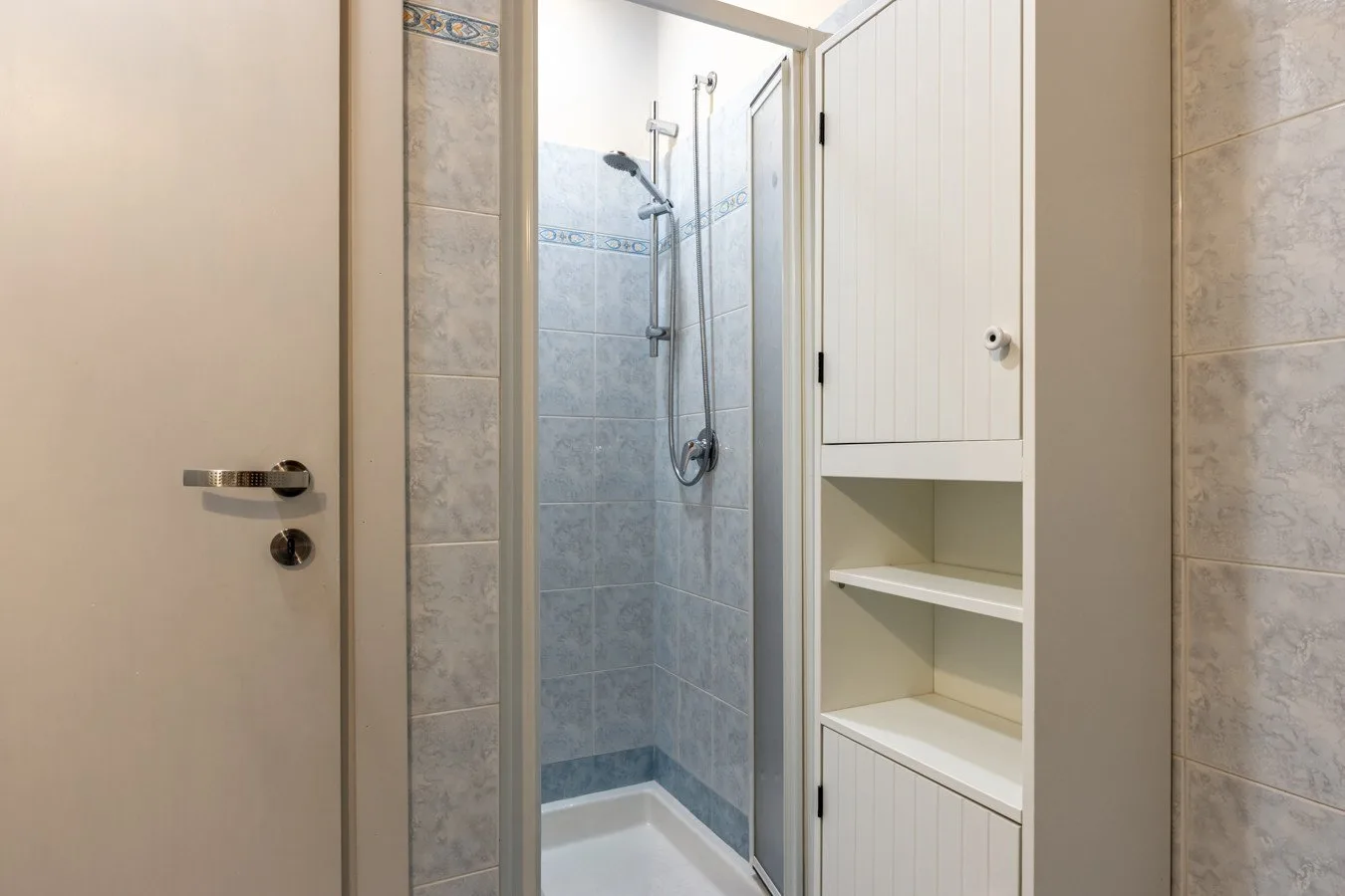 A tiled bathroom with a glass shower and built-in shelving.