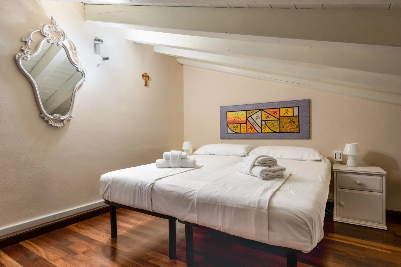 A bedroom with a neatly made bed, folded towels, and colorful wall art.