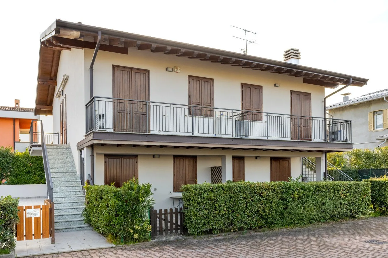 A two-story residential building with a long balcony and a hedge along the front.