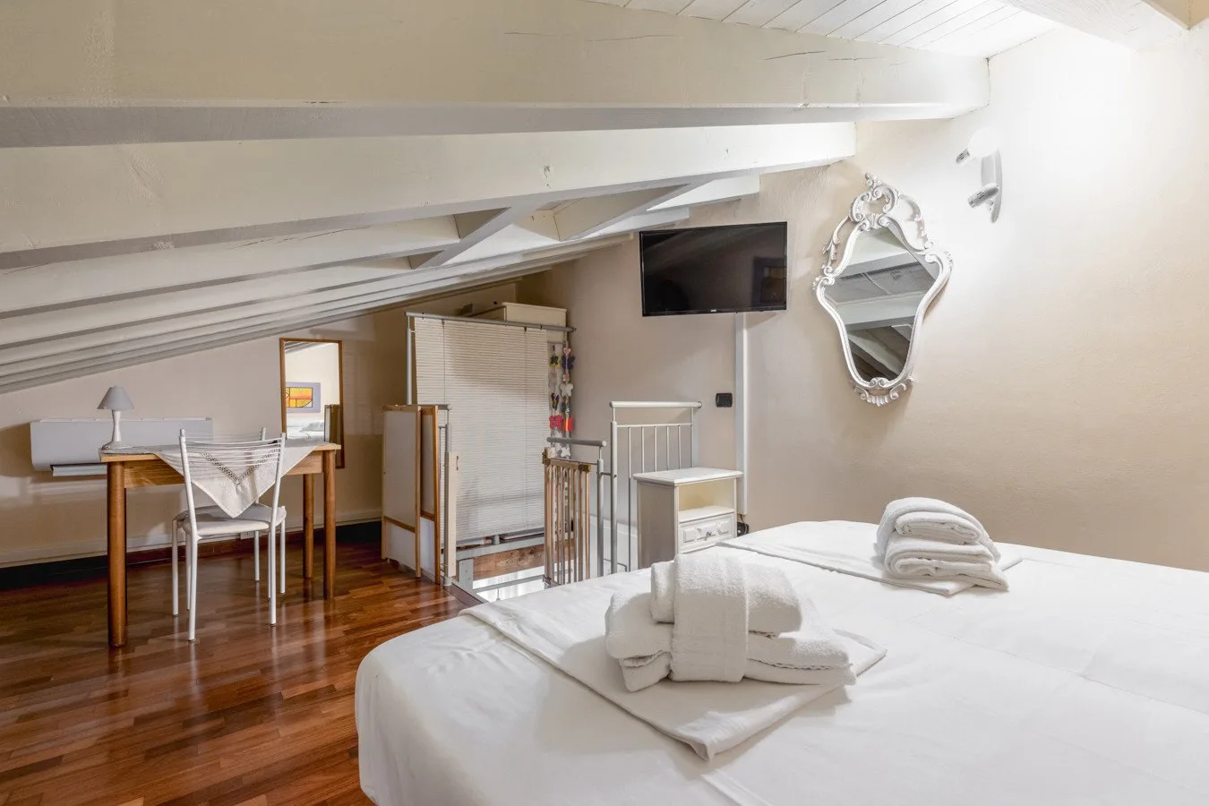 A bedroom with a white bed beneath a sloped ceiling and exposed beams.