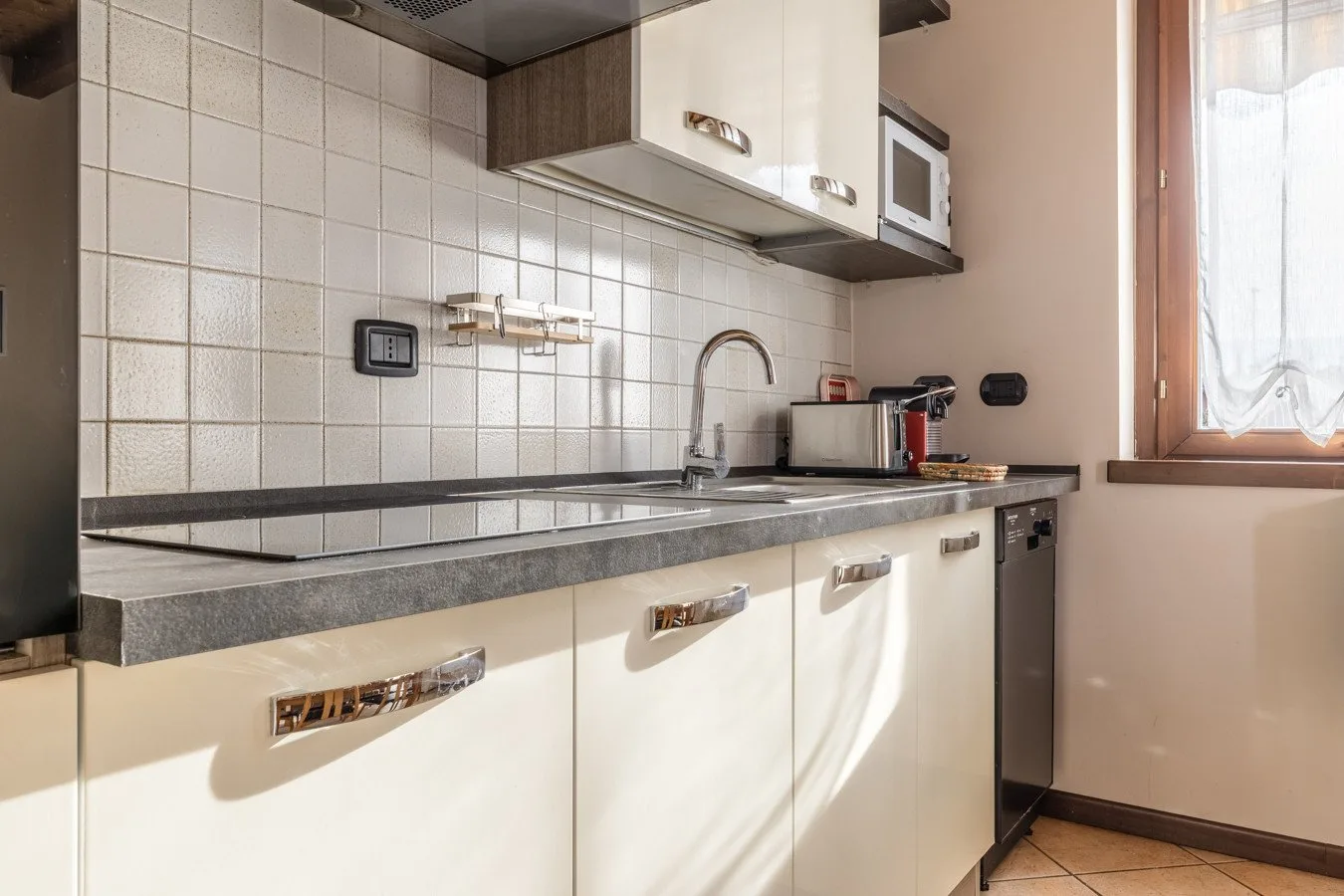A compact kitchen with pale cabinets, a tiled backsplash, and a window.