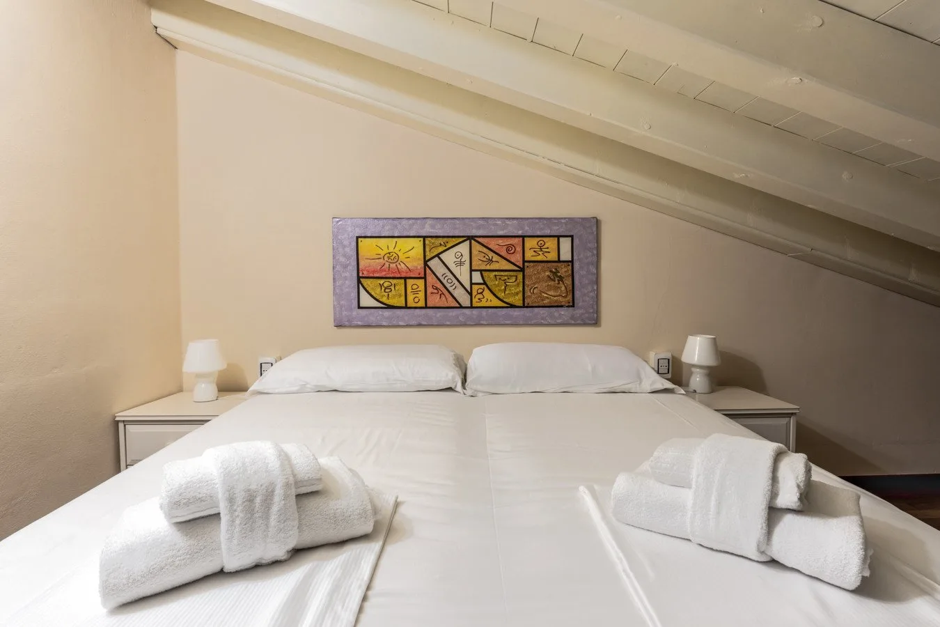 A bedroom with a neatly made bed and colorful artwork above it.