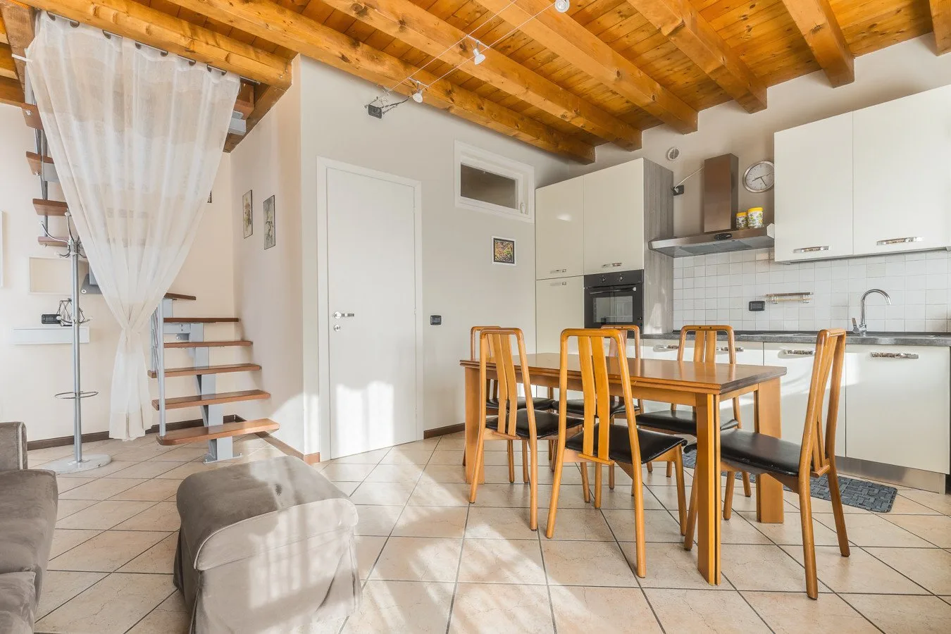 An open kitchen and dining area with a wooden table beneath exposed ceiling beams.