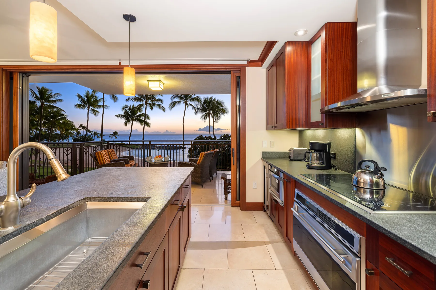 Una cocina se abre a un balcón con palmeras y vistas al agua.