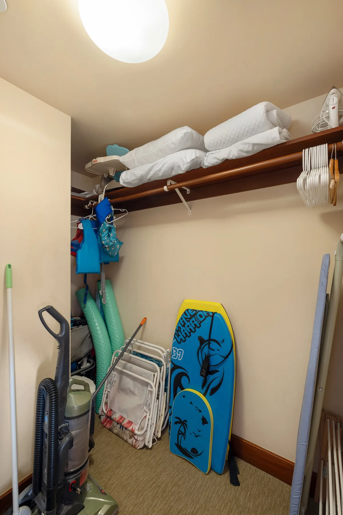 Un armario de almacenamiento tiene ropa de cama doblada en un estante y artículos de playa debajo.