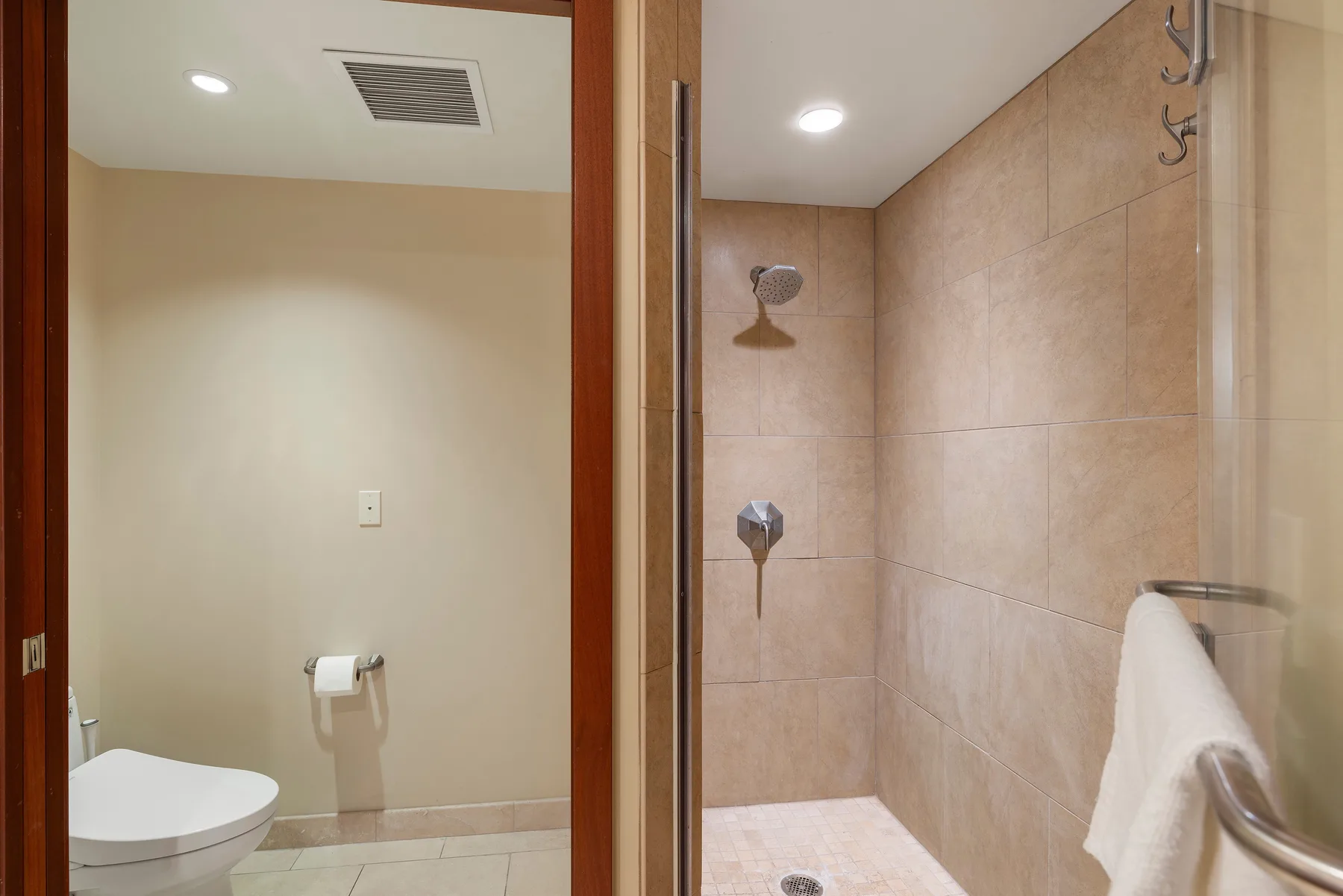 Un baño con azulejos, una ducha y una toalla colgada en el vidrio.
