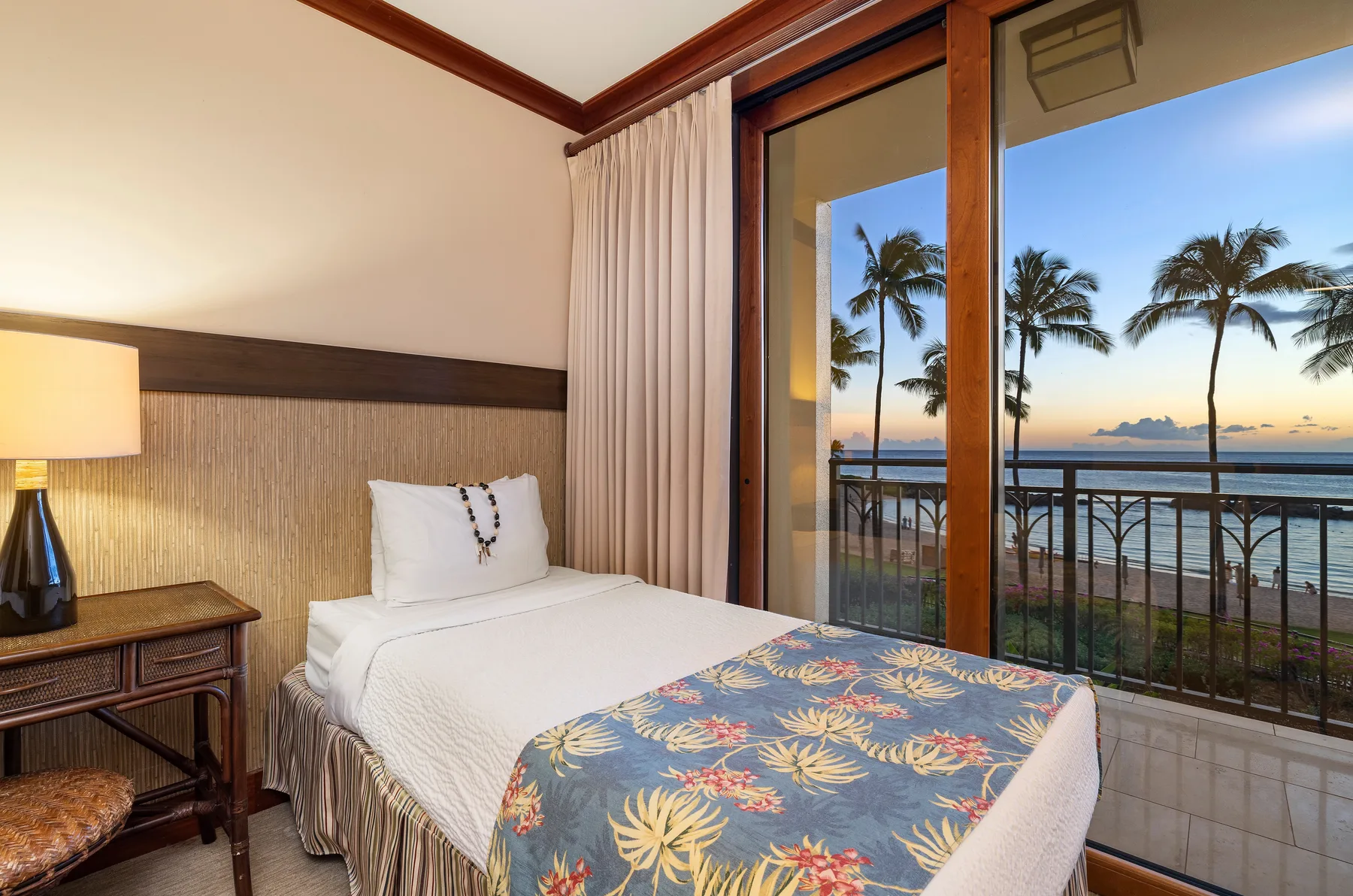 Un dormitorio con una cama bien tendida junto a una ventana amplia con vista a palmeras y agua.