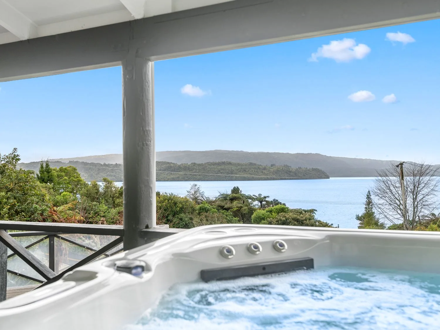 A hot tub on a covered deck overlooking a lake and trees at Splendour on Spencer - Lake Tarawera Holiday Home