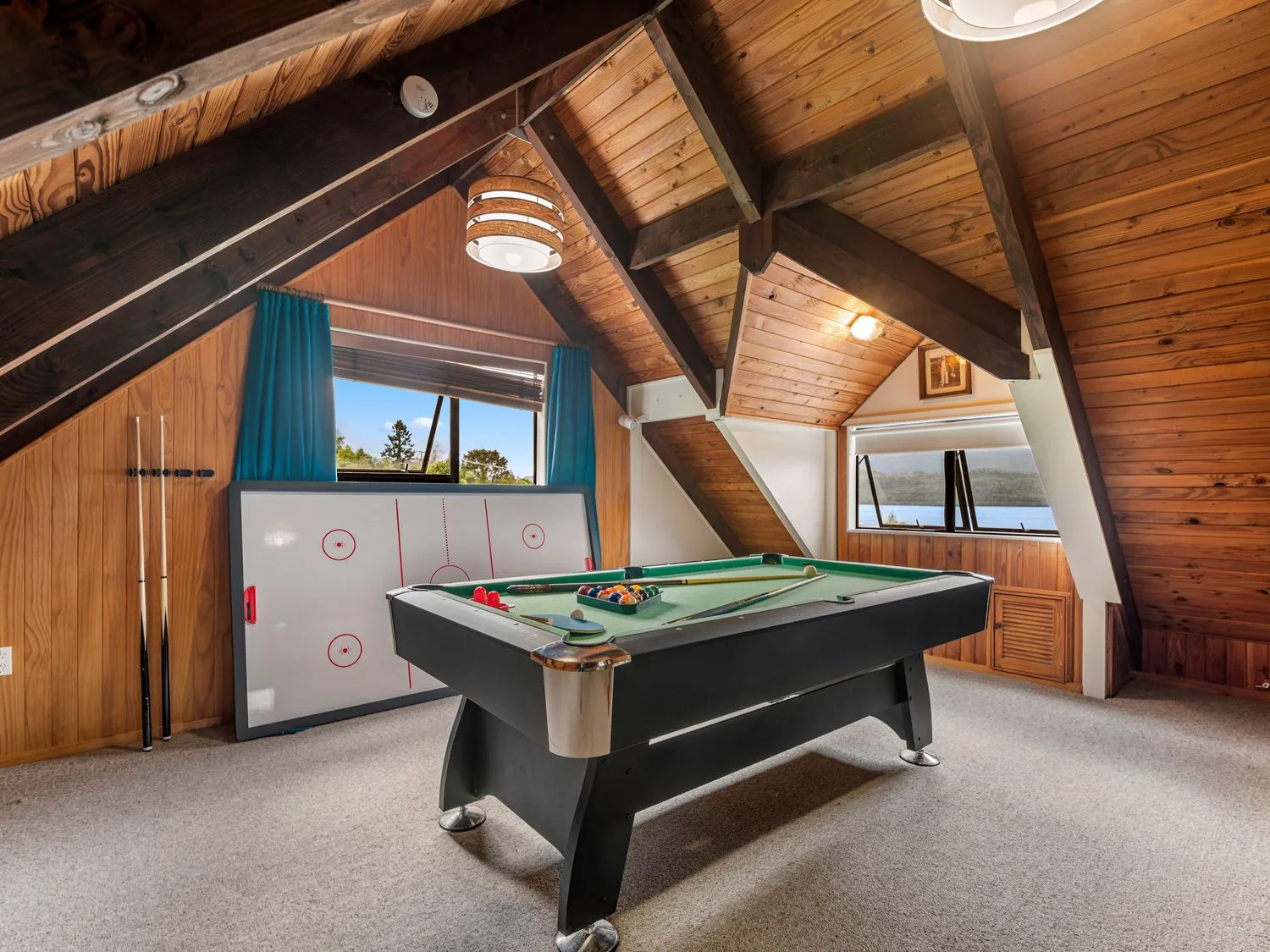 A game room with a pool table, an air hockey table, and windows.