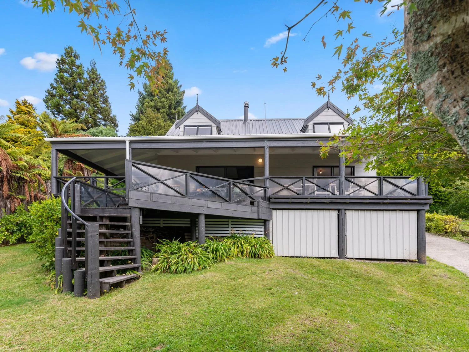 A house exterior with a raised deck, stairs, and trees surrounding the lawn.