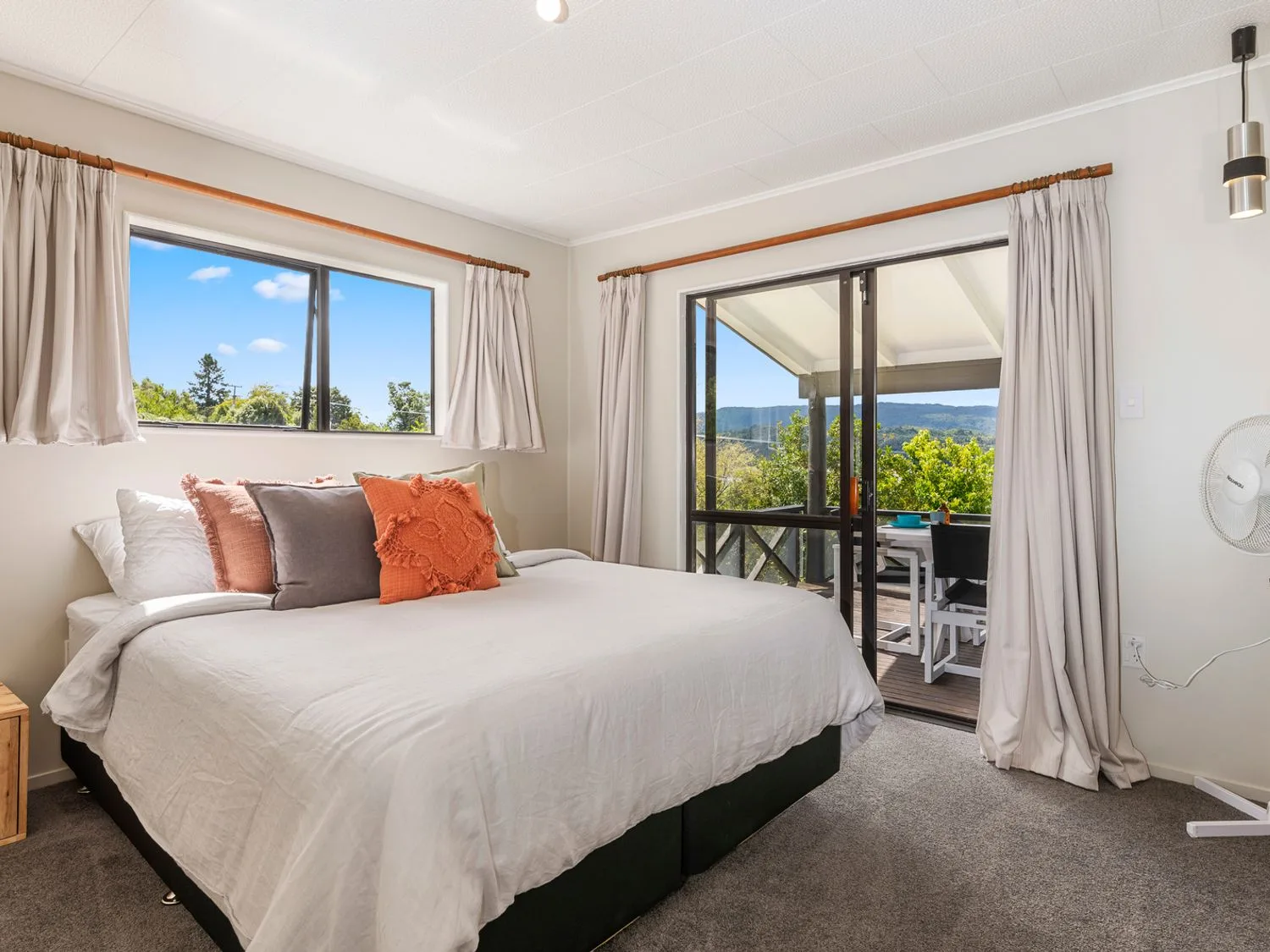 A bedroom with a large bed beside sliding glass doors opening onto a furnished outdoor area.