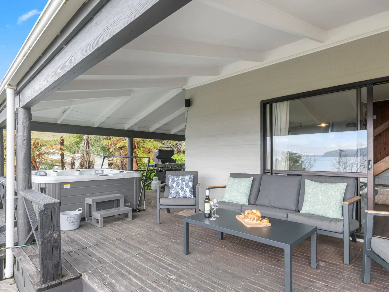 A covered outdoor deck has seating, a hot tub, and a low table with food.