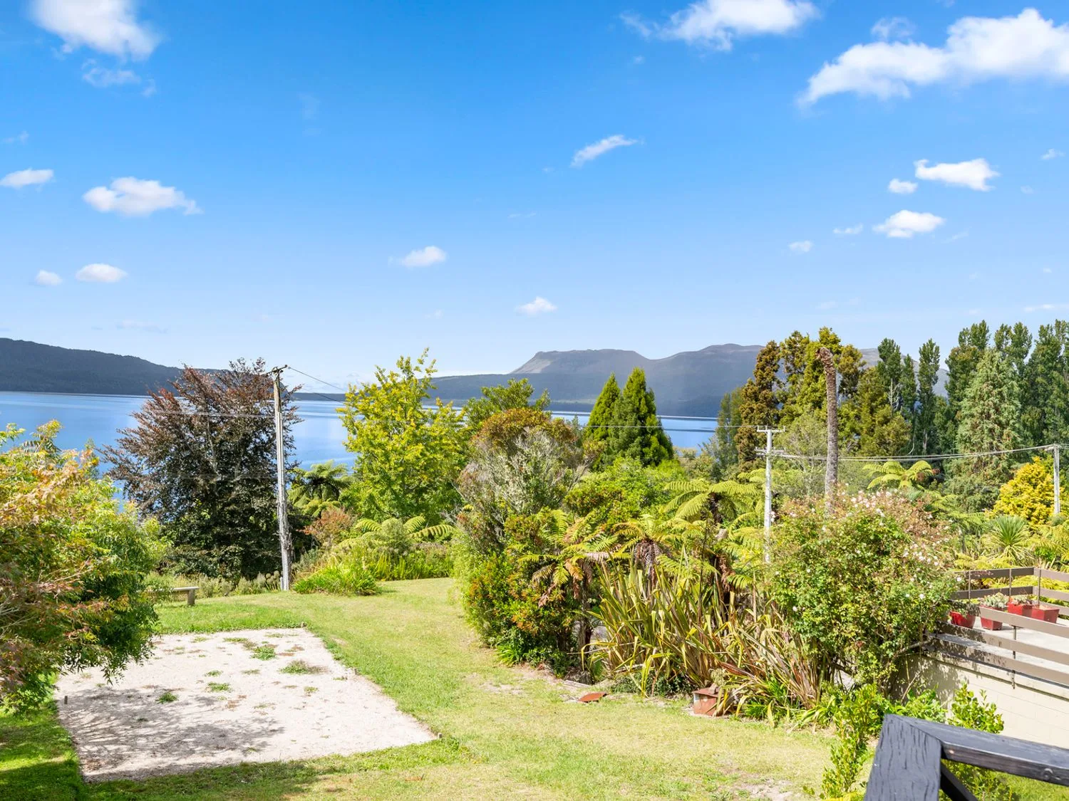 A garden with grass and trees overlooking a lake with hills in the background at Splendour on Spencer - Lake Tarawera Holiday Home in Lake Tarawera