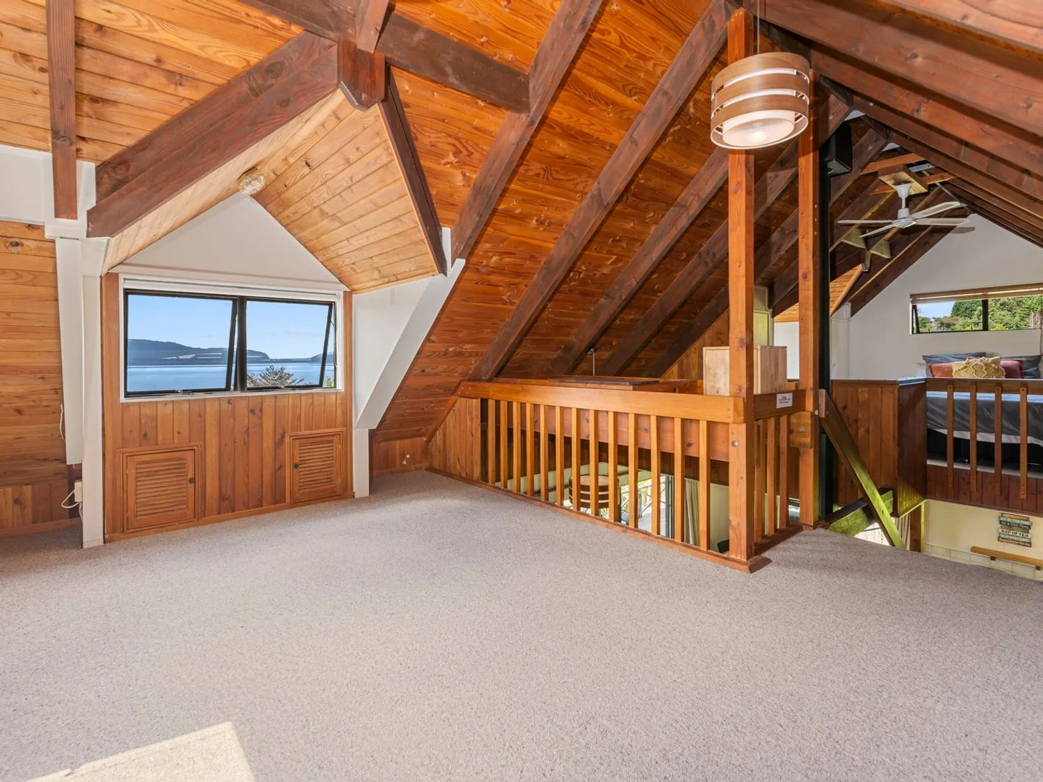 An upper loft area with wood paneling and a window overlooking a lake at Splendour on Spencer - Lake Tarawera Holiday Home