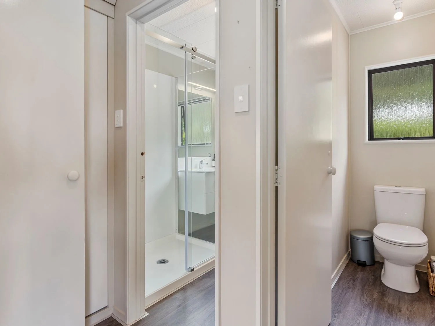A bathroom with a toilet beside a frosted window and an adjacent shower with a glass door at Splendour on Spencer - Lake Tarawera Holiday Home in Lake Tarawera