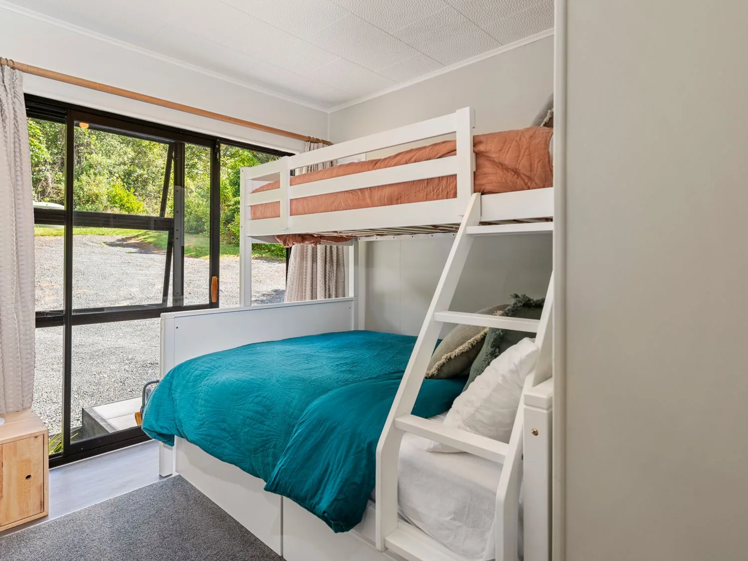 A bedroom with a white bunk bed and sliding glass doors with a view outside at Splendour on Spencer - Lake Tarawera Holiday Home in Lake Tarawera