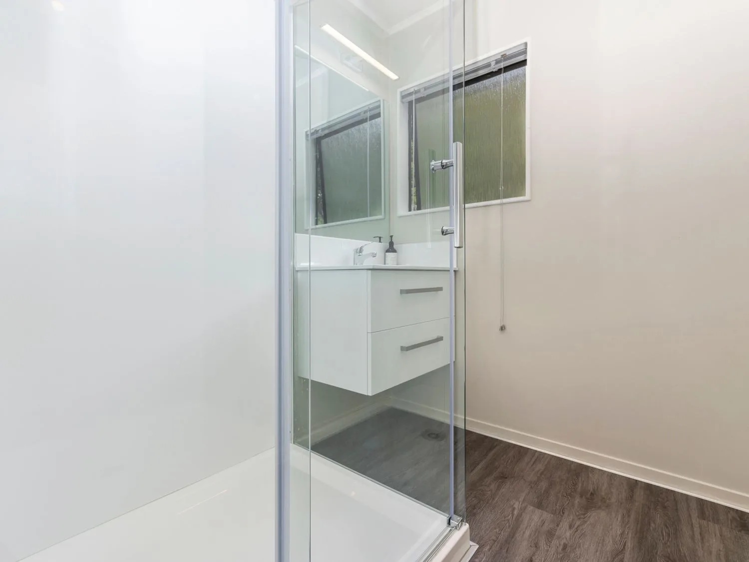 A bathroom with a glass shower and a white floating vanity beneath a mirror.