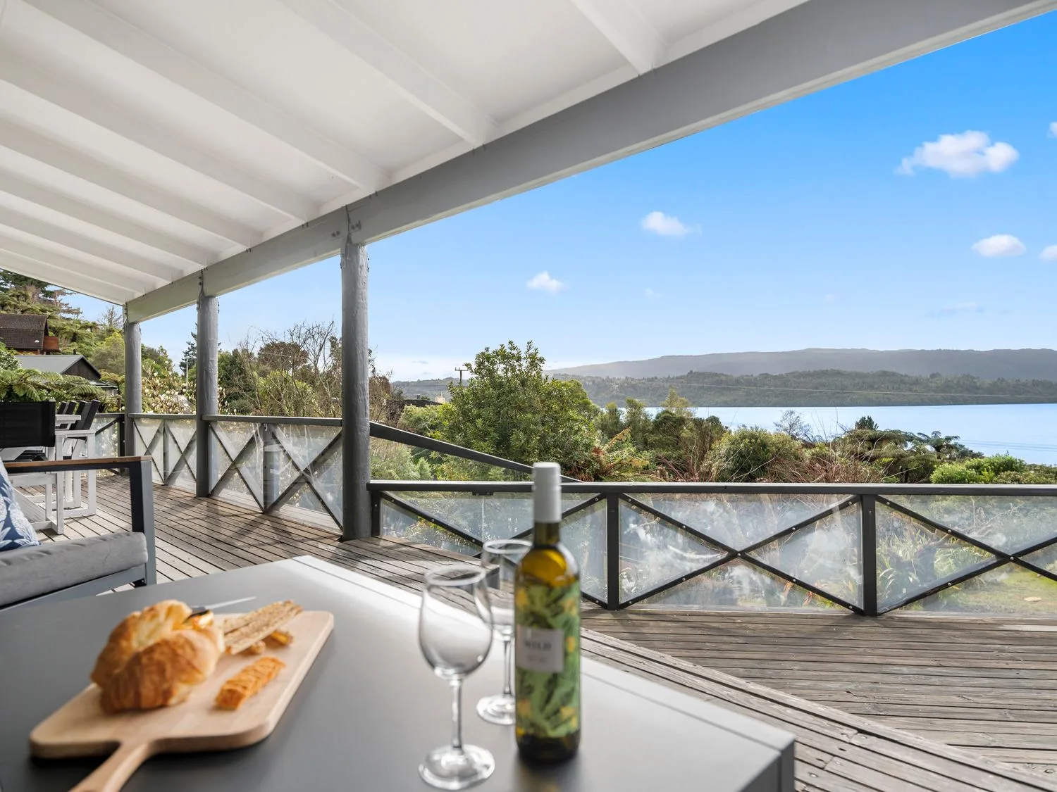 A covered deck with outdoor seating and a table overlooking trees and a lake.