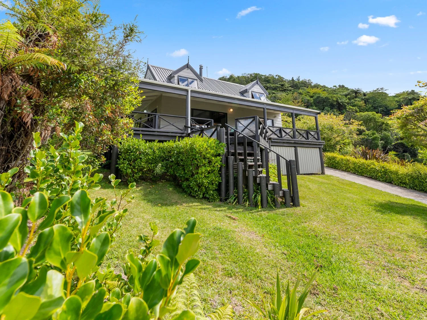 A house with a porch and stairs surrounded by grass and trees at Splendour on Spencer Lake Tarawera