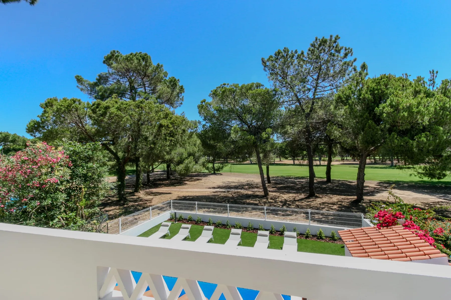 A villa terrace overlooks a pool area and a tree-filled landscape.