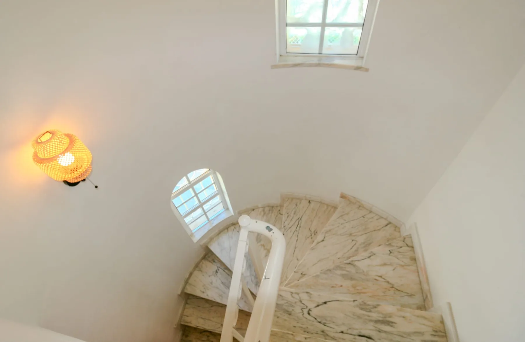 A curved staircase with pale stone steps rises beneath a small window.