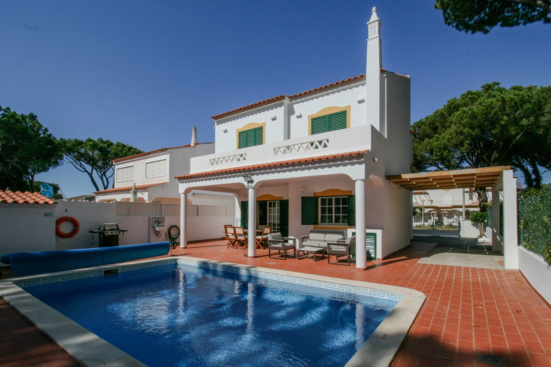 A white villa faces a swimming pool and a tiled patio.