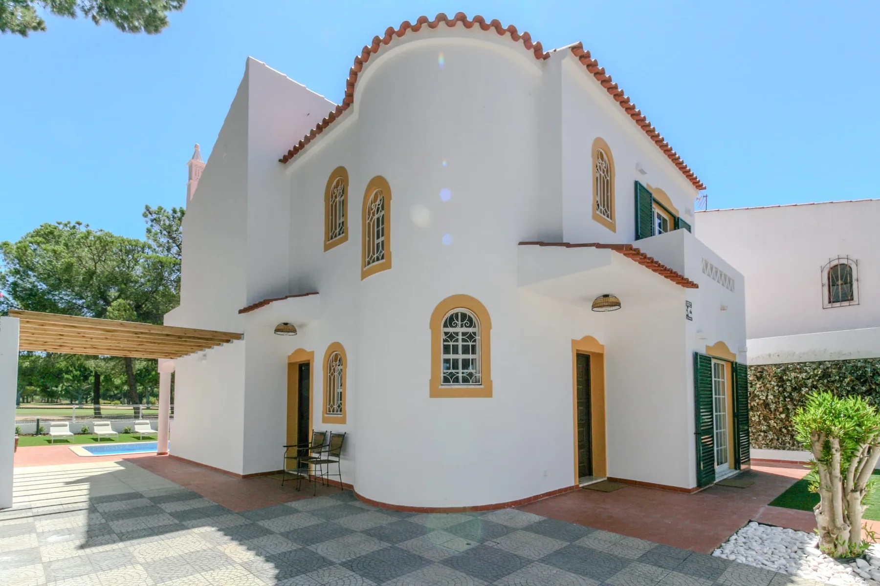 A white two-story house with arched windows stands beside a paved courtyard.