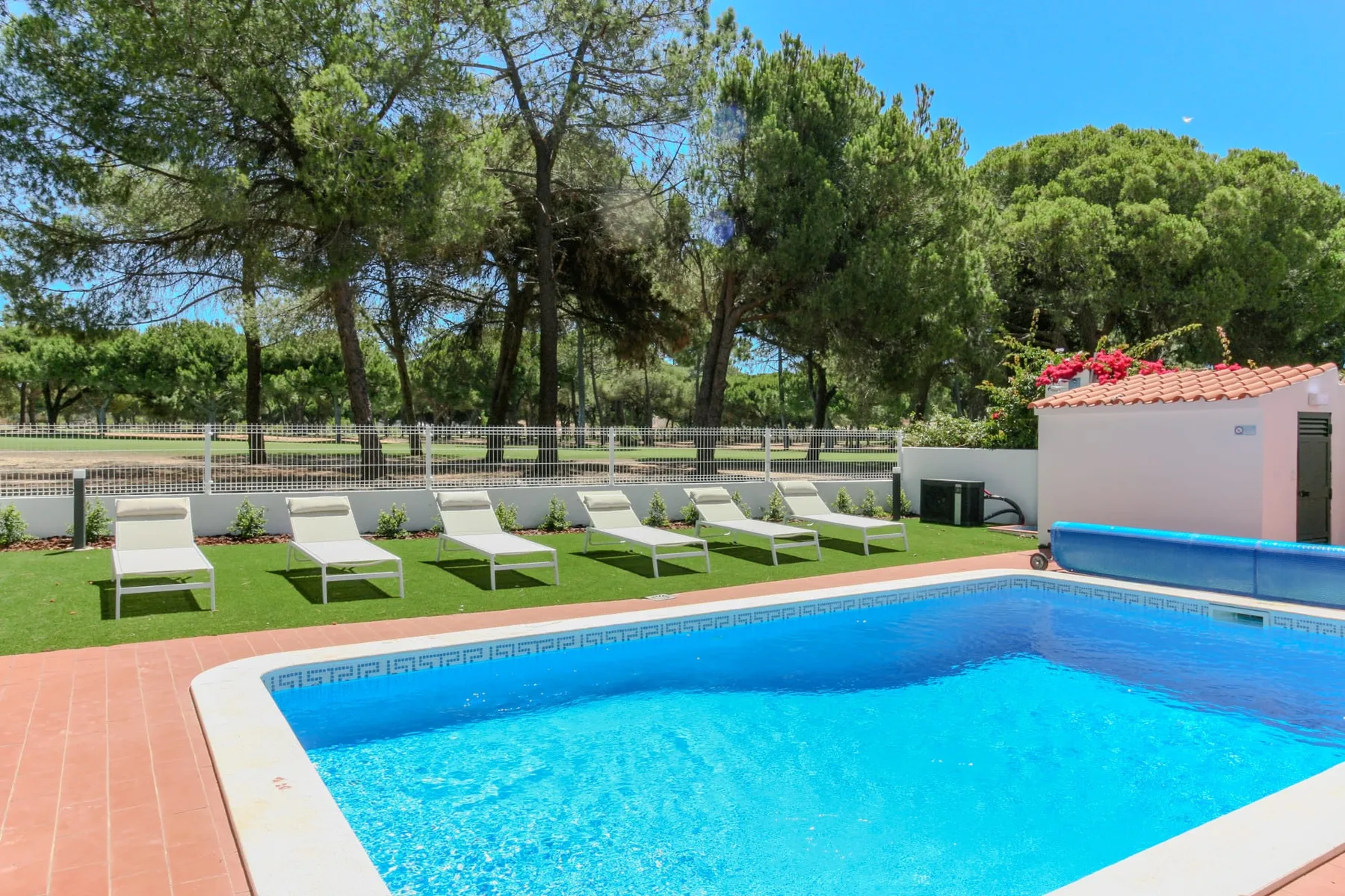 An outdoor swimming pool bordered by a tiled deck and lounge chairs.