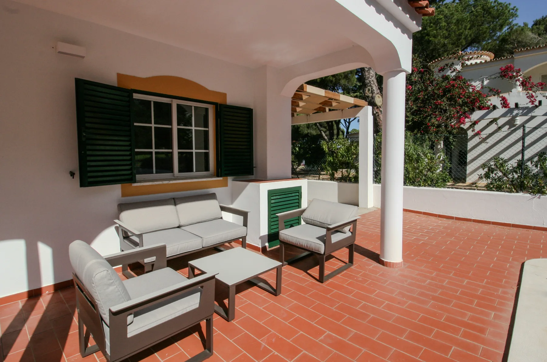 A covered patio with outdoor seating and a window with open shutters.