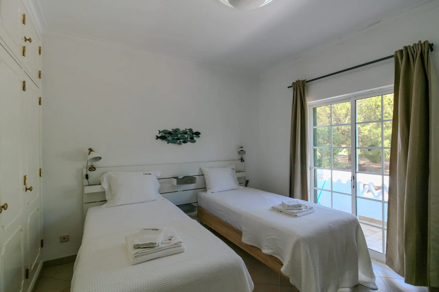 A bright bedroom with two beds and a window overlooking a pool.