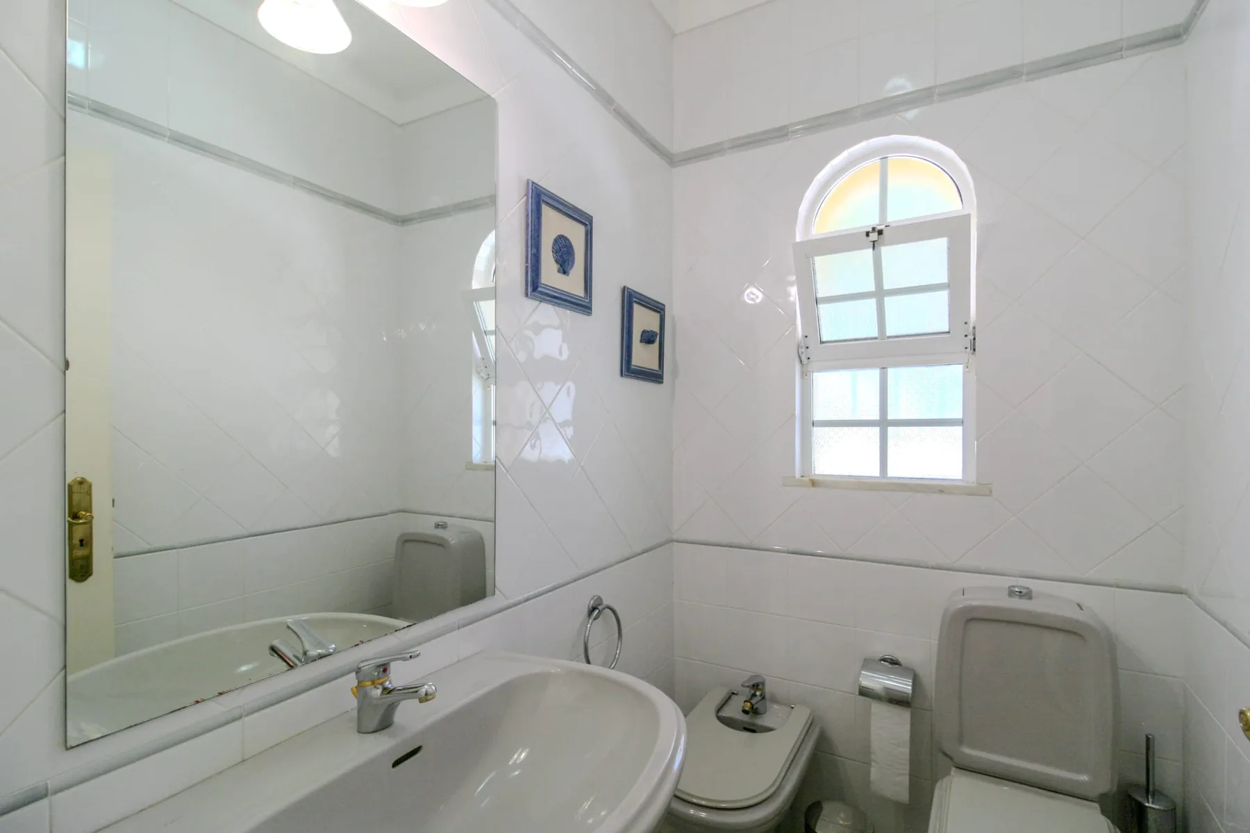 A bright bathroom with a sink, toilet, and arched window.