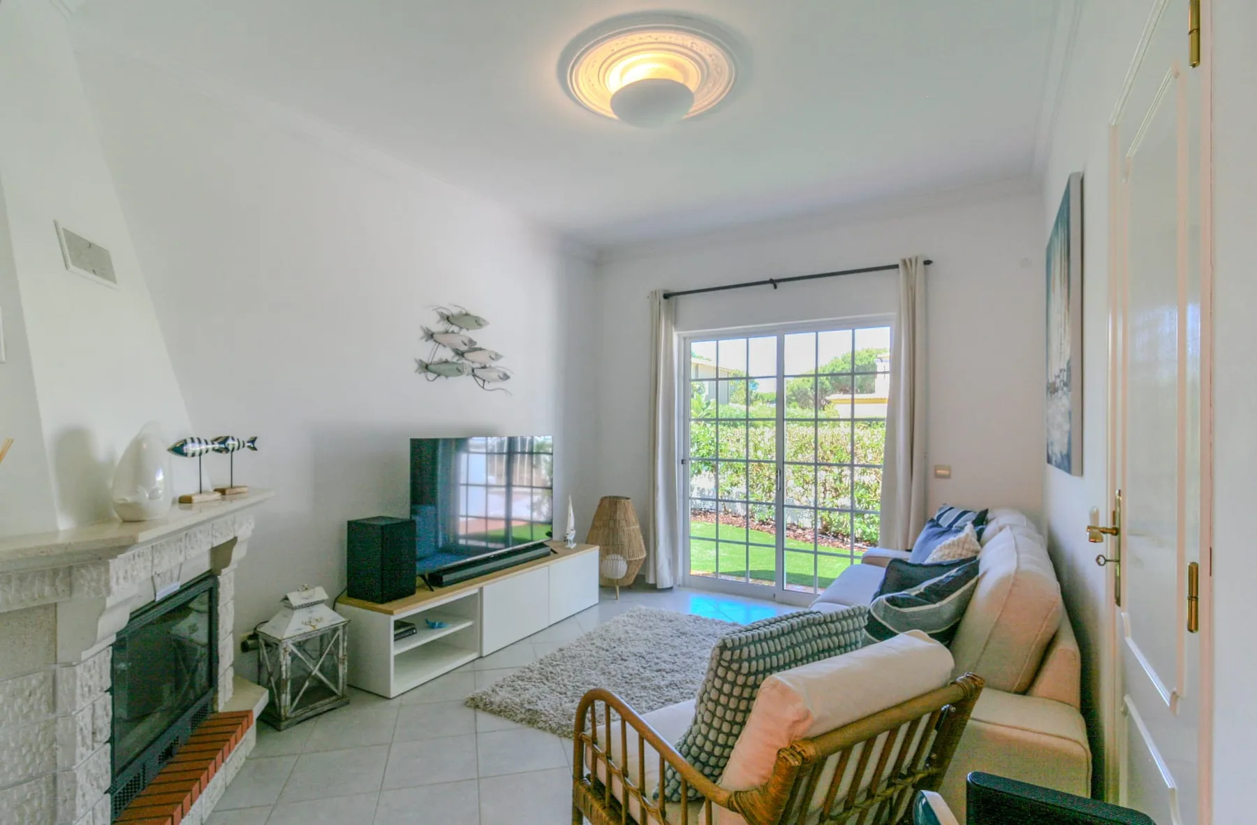 A bright living room with seating, a television, and glass doors opening to greenery.