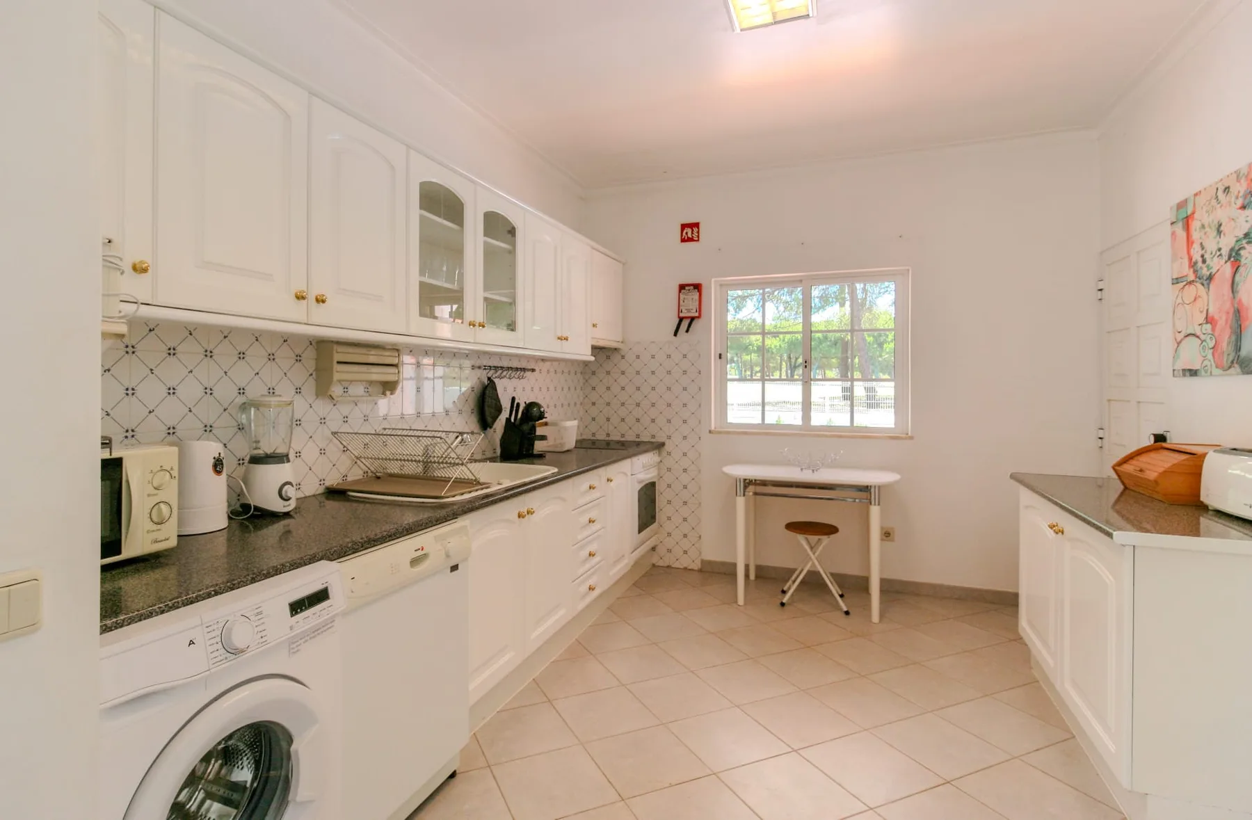 A bright kitchen with white cabinets, counters, and a small table by the window.