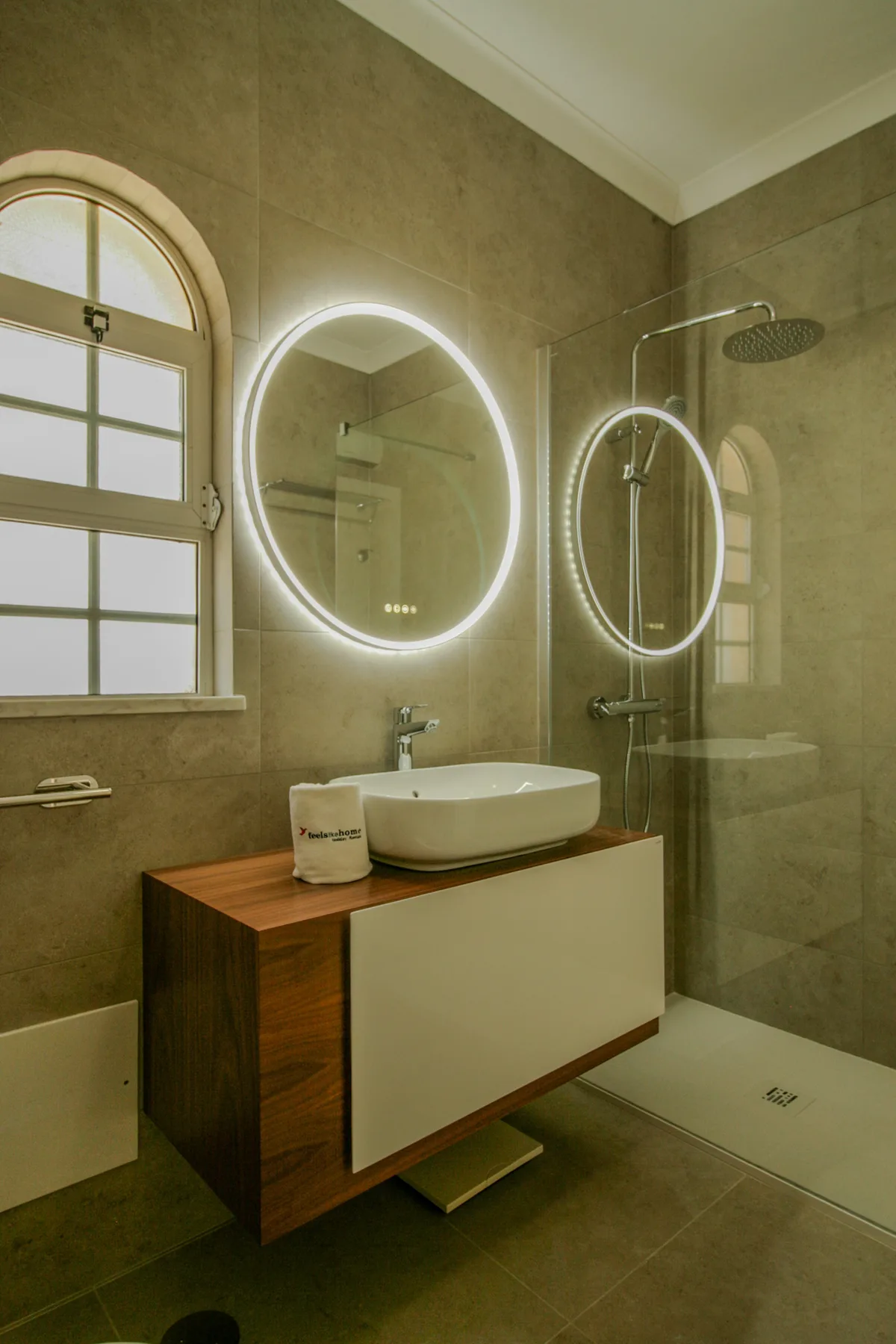 A bathroom with a vessel sink, illuminated mirrors, and a glass shower.