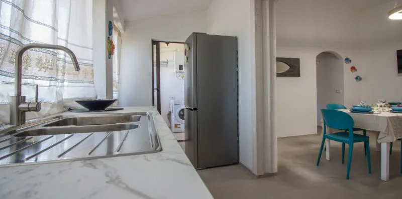 Una cocina se abre a un comedor con una mesa y asientos turquesa.