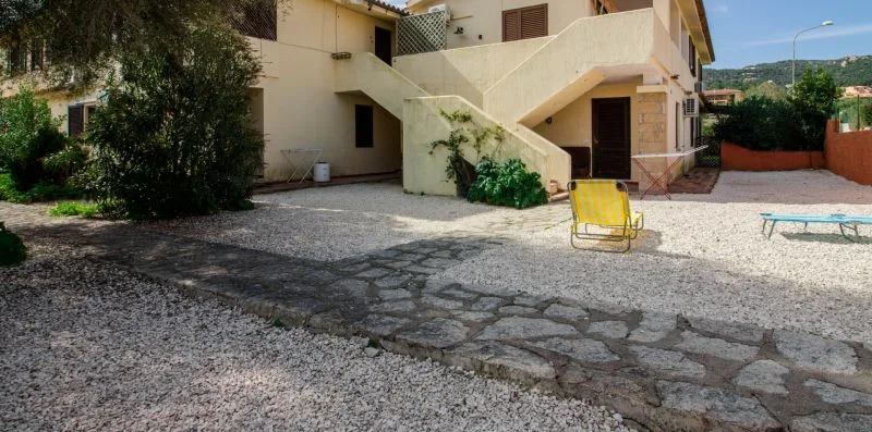 Un patio de grava junto a un edificio claro, con un camino de piedra y asientos al aire libre.