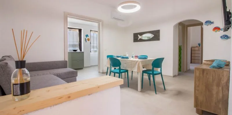 Zona de comedor y estar con una mesa, asientos turquesa y un sofá gris.